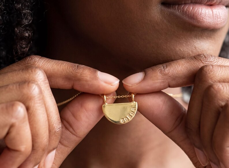 A close-up image of a person's hands holding a gold necklace with a pendant.