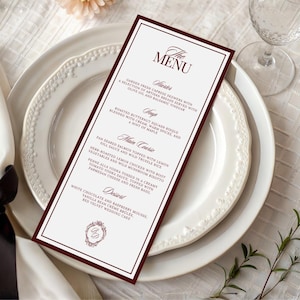 Puede incluir: Una tarjeta de men&uacute; alta y rectangular con un borde burdeos oscuro y fondo blanco. El texto dice THE MENU, seguido de secciones para Starter, Soup, Main Course y Dessert, con varios platos y un peque&ntilde;o monograma circular en la parte inferior.