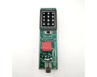 May include: A close-up of a green circuit board with a black keypad and a red component. The board has the text "dapy® Made in France" printed on it.