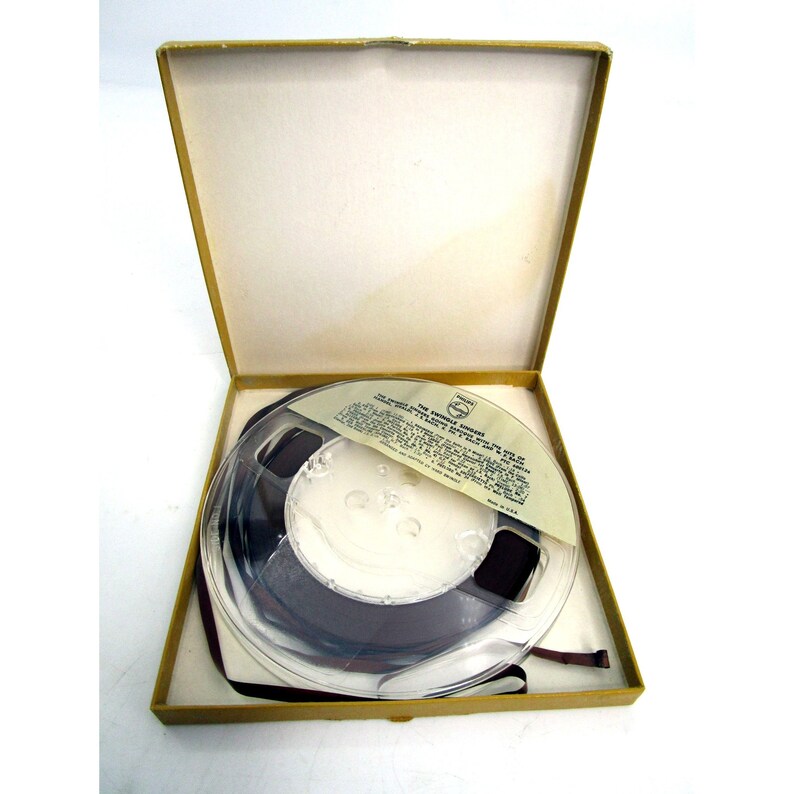 K&ouml;nnte beinhalten: Ein Vintage-Tonband auf einer Spule in einer braunen Pappbox. Das Band ist mit "The Versatile Ambassador, The Story of the Ford Motor Company, 1903-1953" beschriftet.