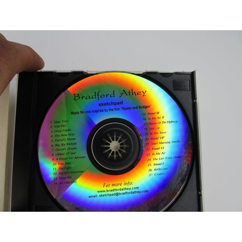 May include: A silver compact disc with a rainbow iridescent effect. The disc has text that reads "Bradford Athey sketchpad Music for and inspired by the film "Roads and Bridges" and lists the track titles.