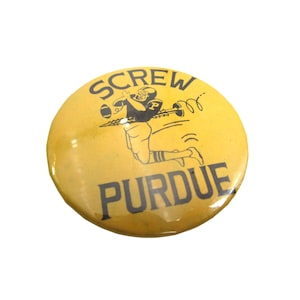 May include: A yellow button with the text "SCREW PURDUE" in black lettering. A cartoon football player is depicted in the center of the button, holding a football and being launched by a screw.