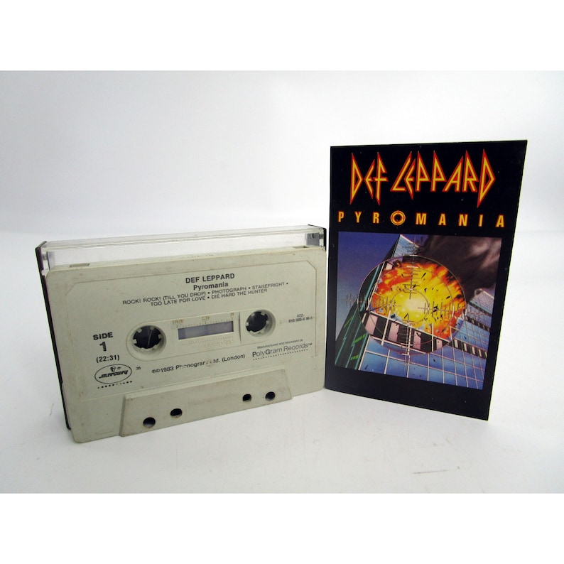 May include: A white cassette tape with a black label. The label has the text "DEF LEPPARD Pyromania" and a list of songs. The cassette tape is next to a black and white album cover with the text "DEF LEPPARD PYROMANIA".