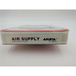 May include: A white cassette tape case with the text "AIR SUPPLY GREATEST HITS" and "ARISTA S134424" printed on it.