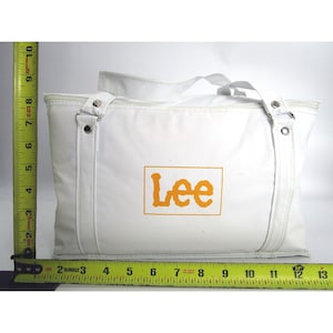 Könnte beinhalten: Weiße Einkaufstasche mit einem großen orangen "Lee"-Logo auf der Vorderseite.