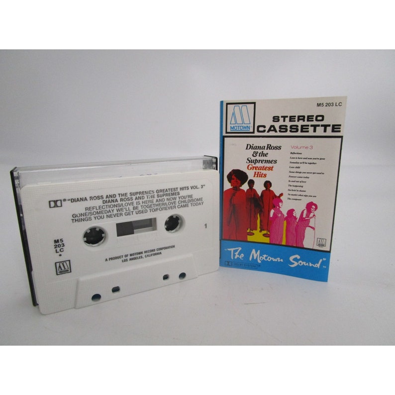 May include: A white cassette tape with a black label that reads "DIANA ROSS AND THE SUPRENES GREATEST HITS VOL. 3" and a black and white Motown logo. The cassette tape is in a clear plastic case. The case has a white label with the text "M5 203 LC" and a black and white Motown logo. The case is next to a white and red album cover with the text "Diana Ross & the Supremes Greatest Hits Volume 3" and a picture of the Supremes.