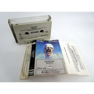 May include: A cassette tape and album cover for the Scorpions' 1982 album "Blackout". The album cover features a man with a microphone in front of a dark background. The cassette tape is labeled "Scorpions Blackout" and has the Mercury Records logo.