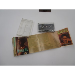 Peut inclure: Une cassette audio de l'album "Makeba" de Miriam Makeba avec une pochette marron et verte représentant une photo de Miriam Makeba. La cassette audio est dans un boîtier en plastique transparent.