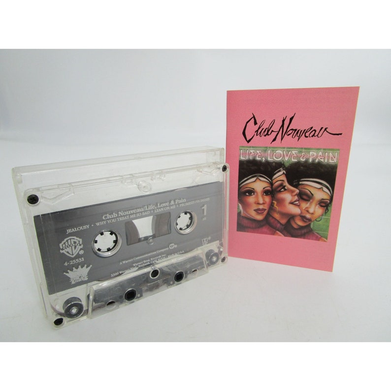May include: A clear cassette tape case with a black cassette tape inside. The cassette tape has the title "Club Nouveau/Life, Love & Pain" printed on it. The cassette tape is next to a pink card with the title "Club Nouveau" and "LIFE, LOVE & PAIN" printed on it.