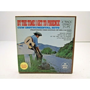 K&ouml;nnte beinhalten: Ein Vintage-Schallplattencover mit einem Cowboy, der auf einer Landstra&szlig;e Gitarre spielt. Der Albumtitel lautet "By The Time I Get To Phoenix" und enth&auml;lt C&W Instrumental Hits von Del Cacher. Das Albumcover ist braun mit einem wei&szlig;en Rand und zeigt ein Foto eines Cowboys in einem braunen Hut und einem blauen Hemd, der Gitarre spielt.