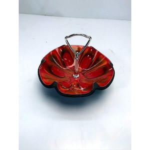 May include: A red and orange ceramic serving dish with a scalloped edge and a silver handle. The dish has a unique swirl pattern.