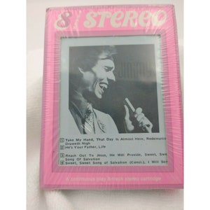 May include: A pink and white 8-track cartridge case with a photo of a man singing into a microphone. The text on the case reads "& STEREO" and lists the songs on the cartridge: "Take My Hand, That Day Is Almost Here, Redemption Draweth Nigh", "He's Your Father, Life", "Reach Out To Jesus, He Will Provide, Sweet, Sweet Song Of Salvation", and "Sweet, Sweet Song of Salvation (Conci.), I Will See". The text at the bottom of the case reads "A continuous play 8-track stereo cartridge".