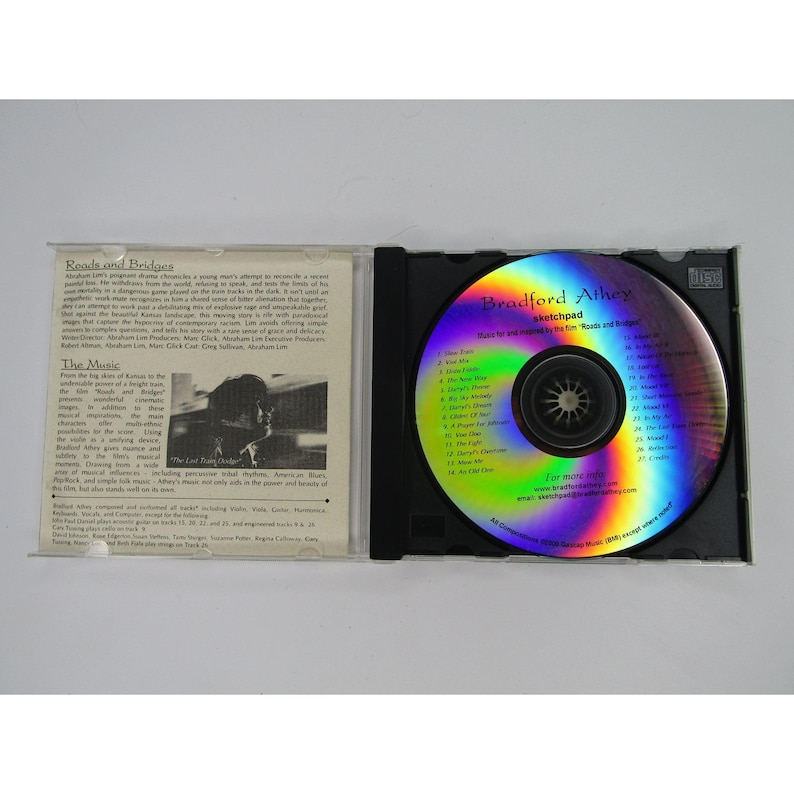 May include: A compact disc with a holographic rainbow effect. The disc is labeled "Bradford Atheys Sketchpad Music for and inspired by the film Roads and Bridges".