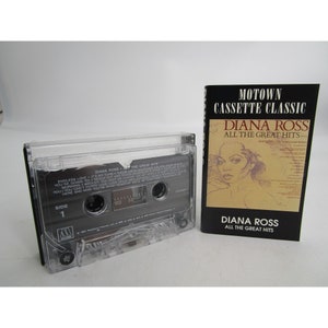 May include: A cassette tape case with a clear plastic cover and a black label. The label says "DIANA ROSS THE GREAT HITS" and has a picture of Diana Ross. The case is next to a black and white cassette tape with a clear plastic cover. The tape label says "DIANA ROSS THE GREAT HITS" and has a picture of Diana Ross. The tape is labeled "SIDE 1" and has a Motown logo.