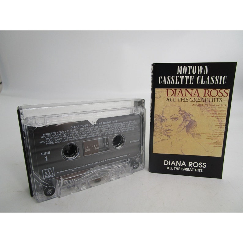 May include: A cassette tape case with a clear plastic cover and a black label. The label says "DIANA ROSS THE GREAT HITS" and has a picture of Diana Ross. The case is next to a black and white cassette tape with a clear plastic cover. The tape label says "DIANA ROSS THE GREAT HITS" and has a picture of Diana Ross. The tape is labeled "SIDE 1" and has a Motown logo.