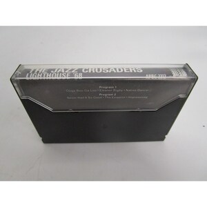 Op de afbeelding: Een zwarte cassetteband met de tekst "THE JAZZ CRUSADERS LIGHTHOUSE '68" en "ARRC 2317" gedrukt op de voorkant. De band vermeldt de nummers "Ooga-Boo Ga-Loo", "Eleanor Rigby", "Native Dancer", "Never Had It So Good", "The Emperor" en "Impressions".