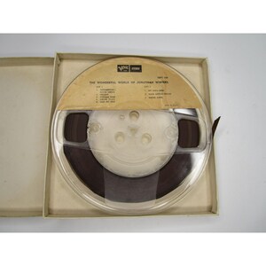 May include: A clear plastic reel with a brown tape inside. The reel is labeled "The Wonderful World of Jonathan Winters" and has a list of songs on each side. The reel is in a white cardboard box.