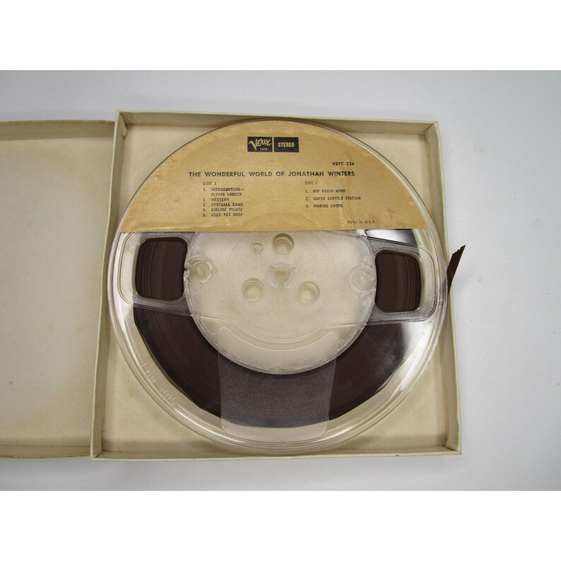 May include: A clear plastic reel with a brown tape inside. The reel is labeled "The Wonderful World of Jonathan Winters" and has a list of songs on each side. The reel is in a white cardboard box.