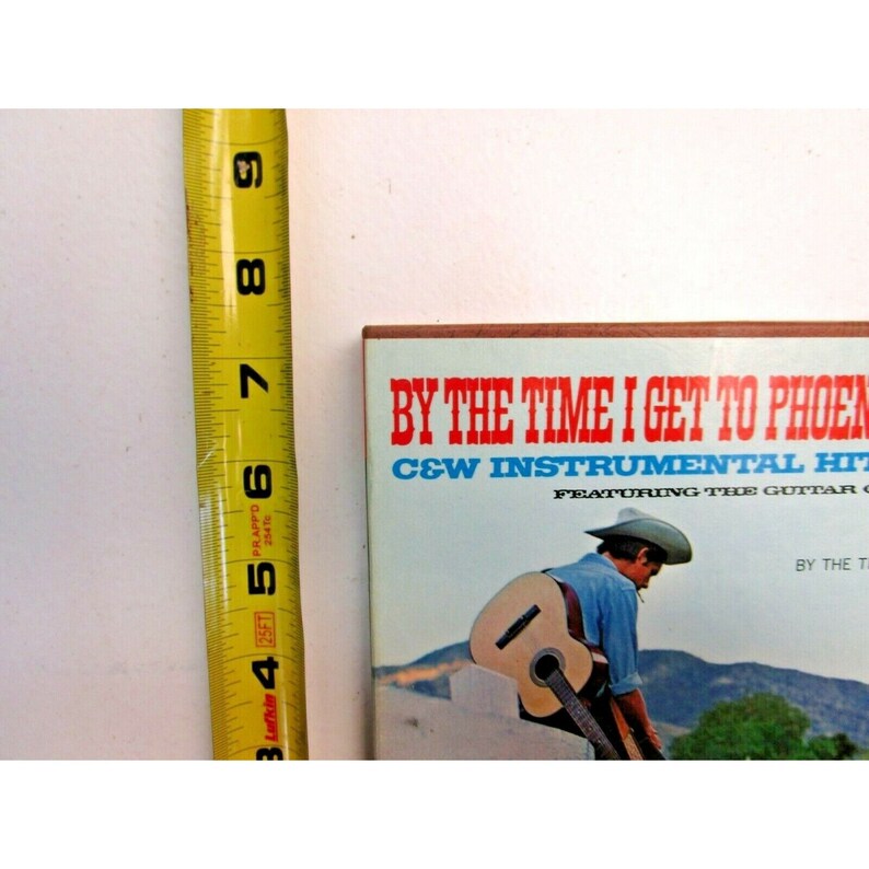 K&ouml;nnte beinhalten: Ein Vintage-Schallplattencover mit blauem Hintergrund und rotem und wei&szlig;em Text, der "By The Time I Get To Phoenix C&W Instrumental Hits Featuring The Guitar Of... By The..." lautet. Ein Mann mit Cowboyhut spielt auf dem Bild Gitarre.