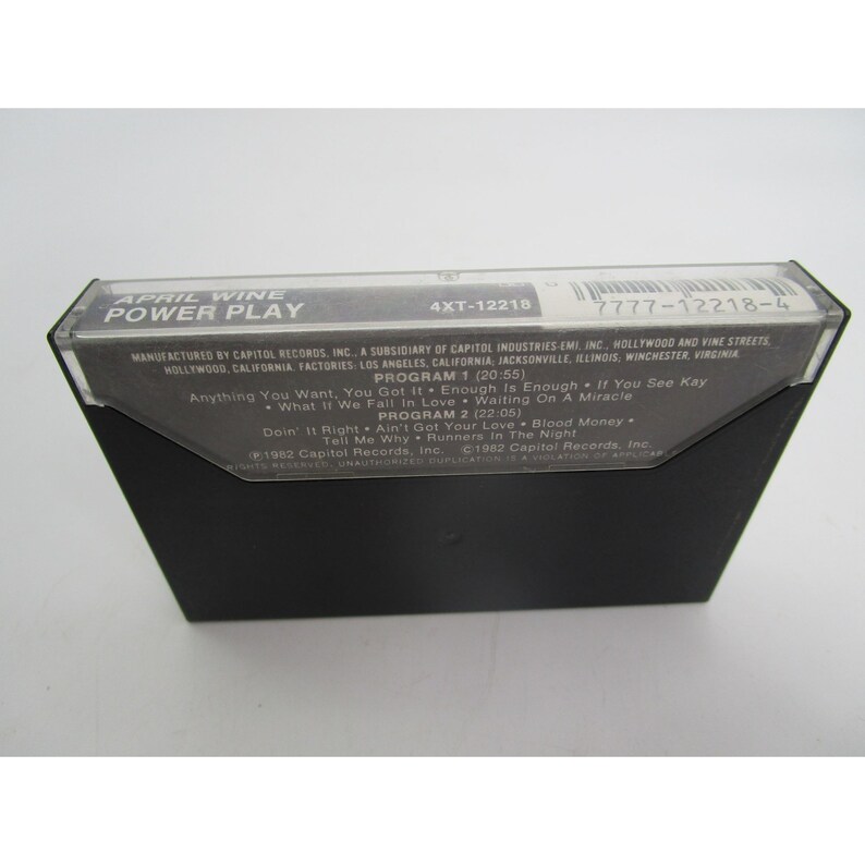 May include: A black cassette tape with a white label. The label has the text "APRIL WINE POWER PLAY" and "4XT-12218" in the top left corner. The label also has the text "7777-12218-4" in the top right corner. The label lists the songs "Anything You Want", "You Got It", "Enough Is Enough", "If You See Kay", "What If We Fall In Love", "Waiting On A Miracle", "Doin' It Right", "Ain't Got Your Love", "Blood Money", "Tell Me Why", "Runners In The Night".
