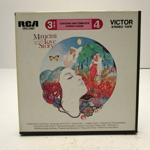 Op de afbeelding: Een witte en roze 8-track cassettehoes met een kleurrijke illustratie van een vrouwengezicht en een vlinder. De hoes is gelabeld "RCA TP3-1067 Mancini The Love Story" en "Victor Stereo Tape".