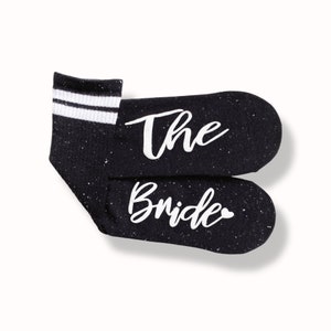 May include: A pair of black socks with white stripes and the words "The Bride" written in white on the socks.