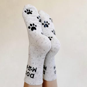 Pu&ograve; includere: Calzini bianchi con impronte di zampe nere e il testo "Dog Mom" sulla caviglia.