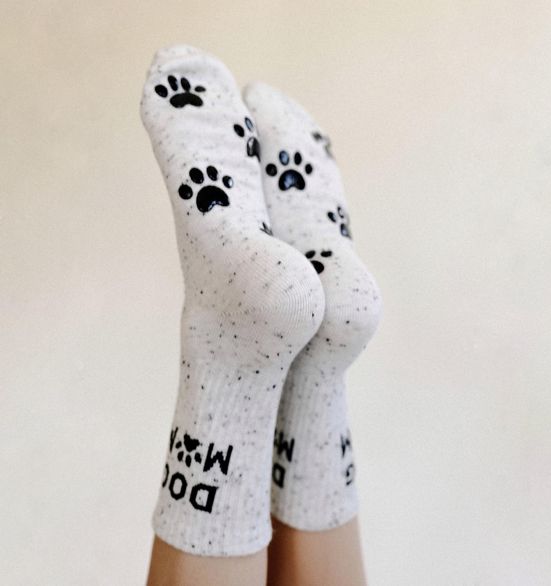 Pu&ograve; includere: Calzini bianchi con impronte di zampe nere e il testo "Dog Mom" sulla caviglia.
