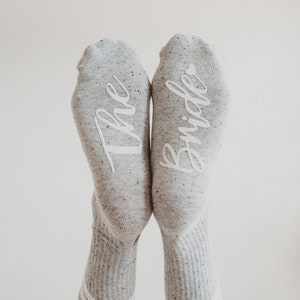 May include: A pair of gray socks with white lettering. One sock says "The" and the other says "Bride".