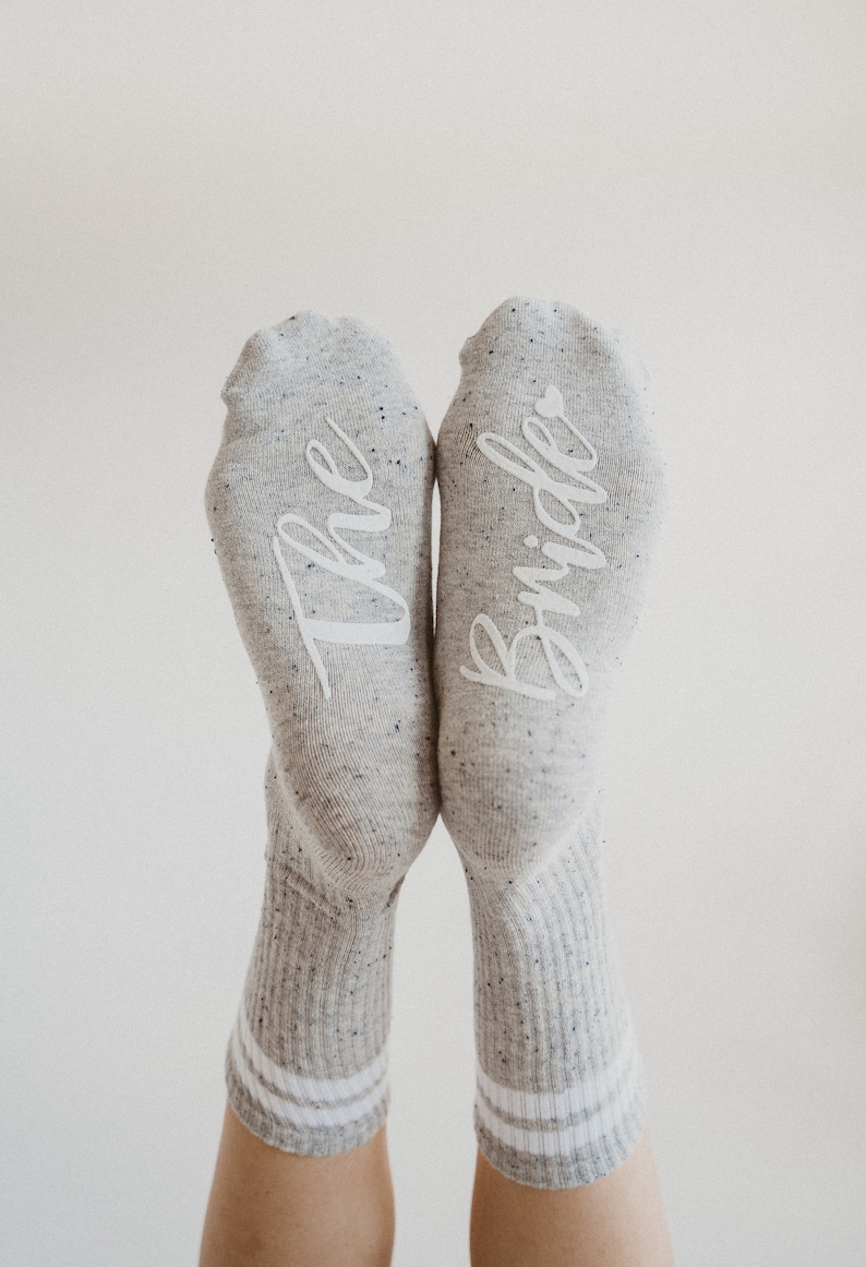 May include: A pair of gray socks with white lettering. One sock says "The" and the other says "Bride".
