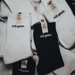 May include: A pile of white and black socks with the text "Blissful Socks" and "end game." embroidered on them.