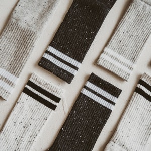May include: Six pairs of socks with a speckled pattern in white and black. The socks have a white stripe with a black stripe on the top of the sock.