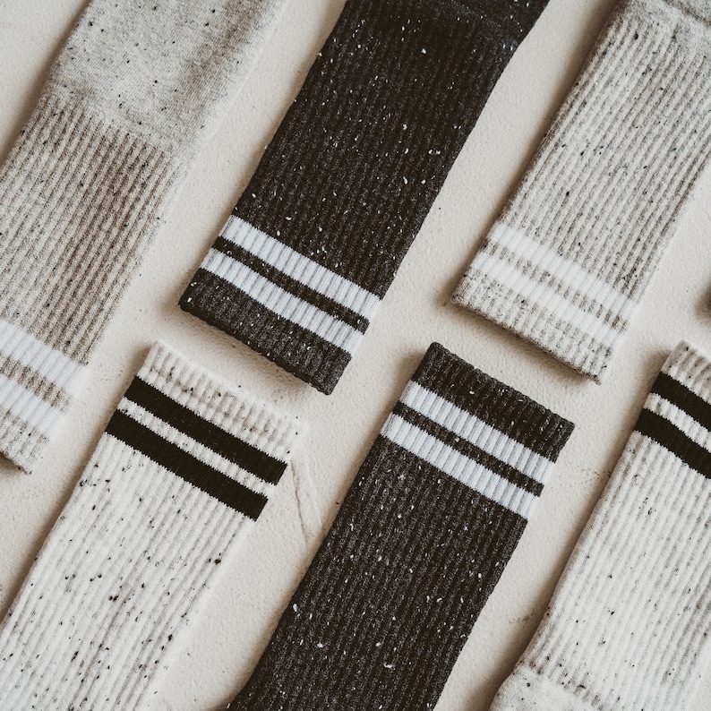 May include: Six pairs of socks with a speckled pattern in white and black. The socks have a white stripe with a black stripe on the top of the sock.