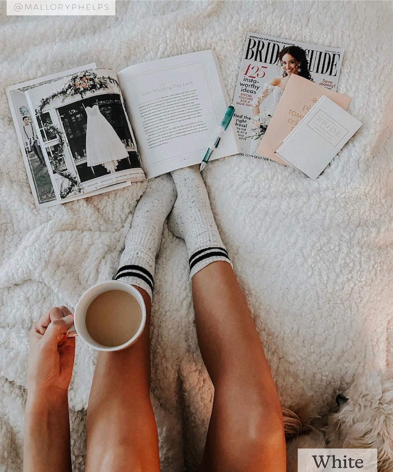 May include: A white fuzzy blanket with a person wearing white socks with black stripes and holding a white coffee mug. The person is reading a magazine about weddings with the text "Bride Guide" and "125 Insta-worthy Ideas".