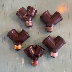 May include: Five vintage brown Y-shaped light bulb sockets. Each socket has two openings for bulbs and a standard screw-in base. The sockets are arranged on a light green surface.