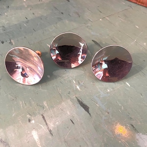 Peut inclure: Trois boutons de meuble circulaires argentés et brillants. Chaque bouton a une surface réfléchissante et une petite cheville en bois à l'arrière. Les boutons sont disposés sur une surface verte et grise.