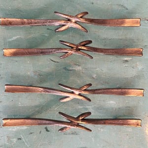 May include: Four bronze-colored metal drawer pulls. Each pull has a rectangular bar with a decorative, star-like element in the center. The pulls are arranged in a vertical pattern against a green background.