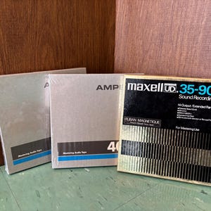 May include: Three vintage audio recording tape boxes. The boxes are silver with black and blue accents. One box features the text "maxell UD 35-90 Sound Recording Tape". The other boxes have the text "AMPE" and "Mastering Audio Tape".
