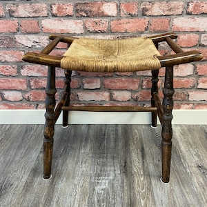 May include: A dark brown wooden stool with a woven rush seat. The stool has turned legs and a simple design.