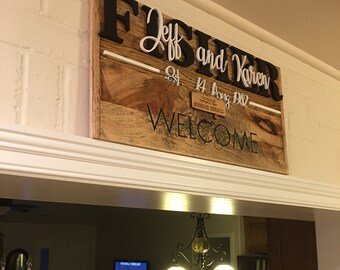 May include: A rustic wooden sign with the text "Fisher Jeff and Karen Est. 14 Aug 1982 Welcome" in black and white lettering.