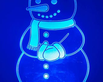 May include: A blue-lighted snowman night light. The snowman has a hat, scarf, and buttons. The light has a power button on the base. A festive and decorative item for the holiday season.