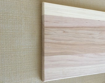 May include: A close-up of a light brown wooden board with a natural wood grain pattern. The board is made of multiple pieces of wood that have been joined together.