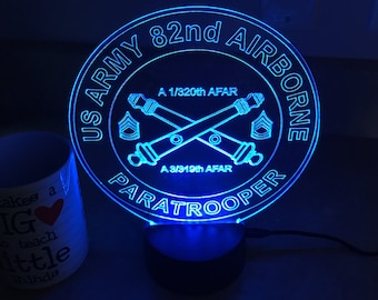 May include: A blue illuminated sign with the text "US ARMY 82nd AIRBORNE PARATROOPER" and crossed cannons with the text "A 1/320th AFAR" and "A 3/919th AFAR".