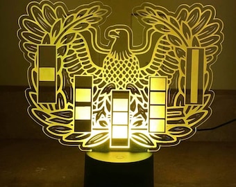 May include: A yellow acrylic night light shaped like the US Army's eagle insignia. The eagle is holding a shield with five stripes. The night light is on a black base.