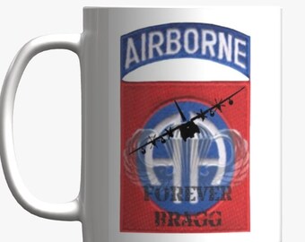 May include: White ceramic mug with a red, white and blue graphic of a military patch. The patch features a blue arch with the word "AIRBORNE" in white letters. The patch also features a red background with a white parachute symbol and the words "FOREVER BRAGG".