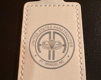 May include: A white leather keychain with a silver key ring. The keychain features a circular emblem with the text "UNITED STATES PARATROOPER" and "FT. BRAGG, NC". The emblem includes a parachute and wings.