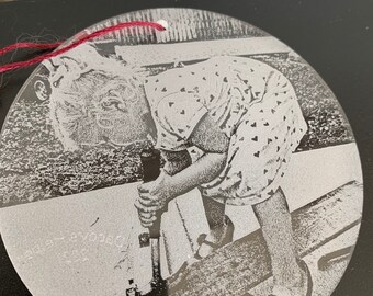 May include: A black and white photograph of a young girl wearing a dress with a heart pattern, standing on a wooden surface and holding a tool.