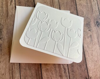May include: White card with an embossed design of white tulips on a white background.