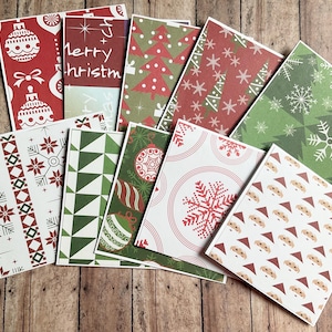 Könnte beinhalten: Eine Sammlung von zehn rechteckigen Grußkarten mit verschiedenen Weihnachtsmustern, darunter rot-weiße Christbaumkugeln, grüne Tannenbäume, Schneeflocken, geometrische Formen und ein sich wiederholendes Muster von Weihnachtsmann-Gesichtern.