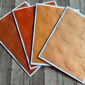 May include: Four blank greeting cards with an embossed pumpkin pattern. The cards are in shades of orange, brown, and tan.